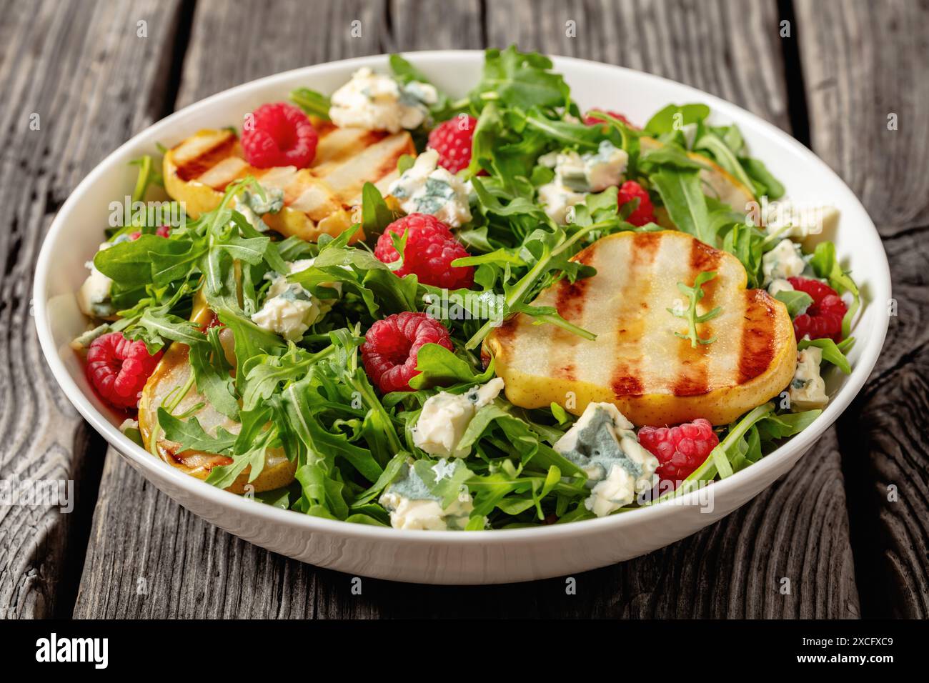 salade de poires grillées avec fromage bleu, roquette et framboises fraîches mûres dans un bol blanc sur une table en bois rustique, gros plan Banque D'Images