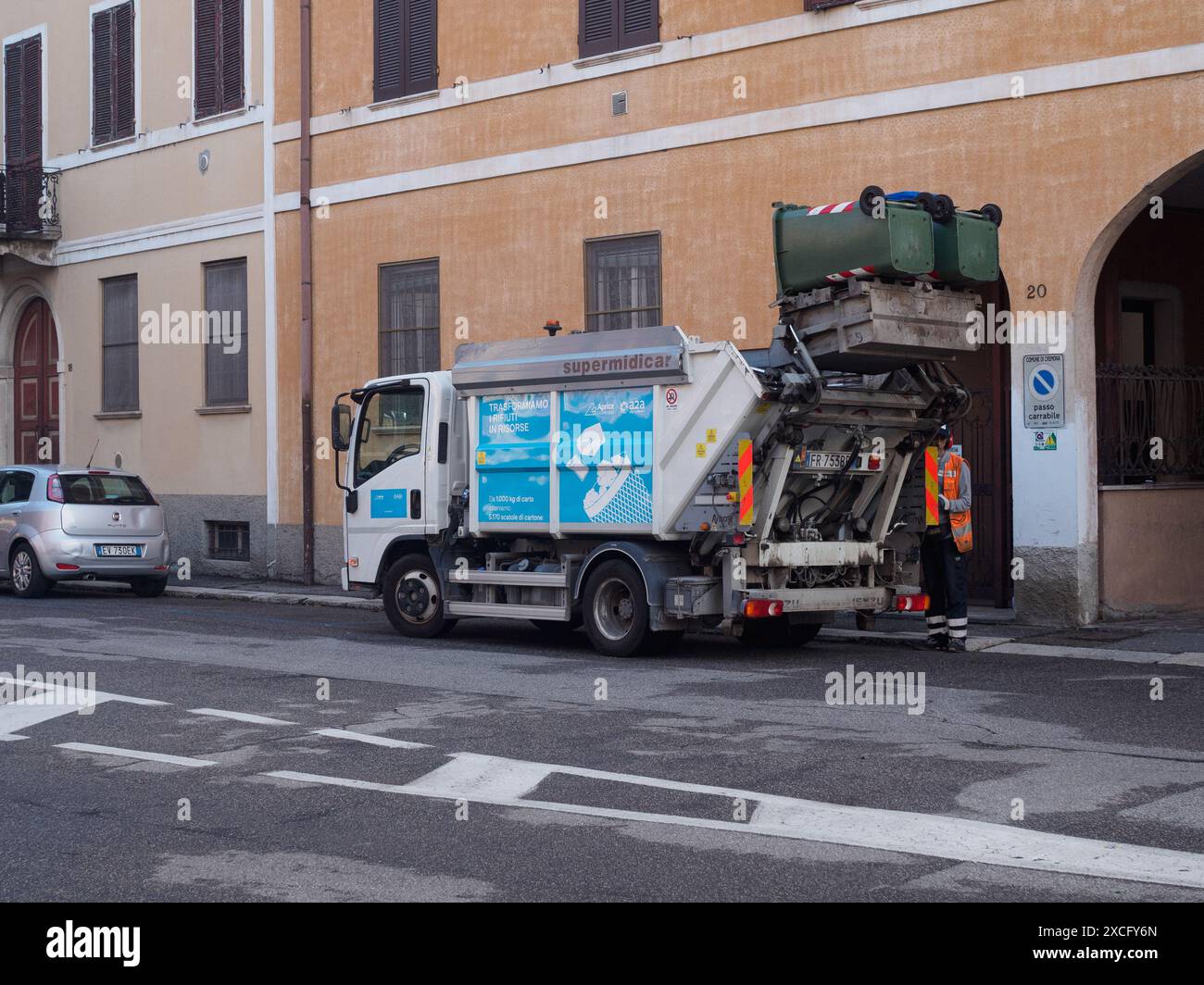 Cremona, Italie - 10 juin 2024 camion à ordures ramassant des poubelles avec un travailleur de l'assainissement attendant à côté dans une rue urbaine Banque D'Images