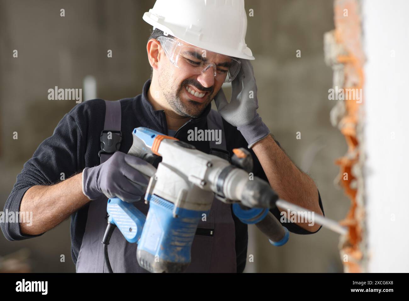 Travailleur de Cosntruction souffrant de maux de tête travaillant avec un mur de démolition d'outil bruyant Banque D'Images