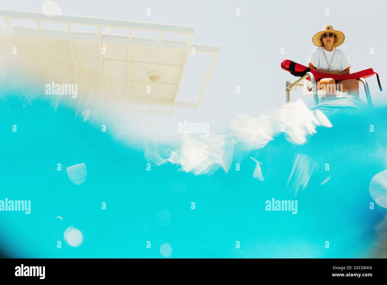 Une jeune dame est assise sur une échelle de piscine avec un chapeau de soleil. Banque D'Images