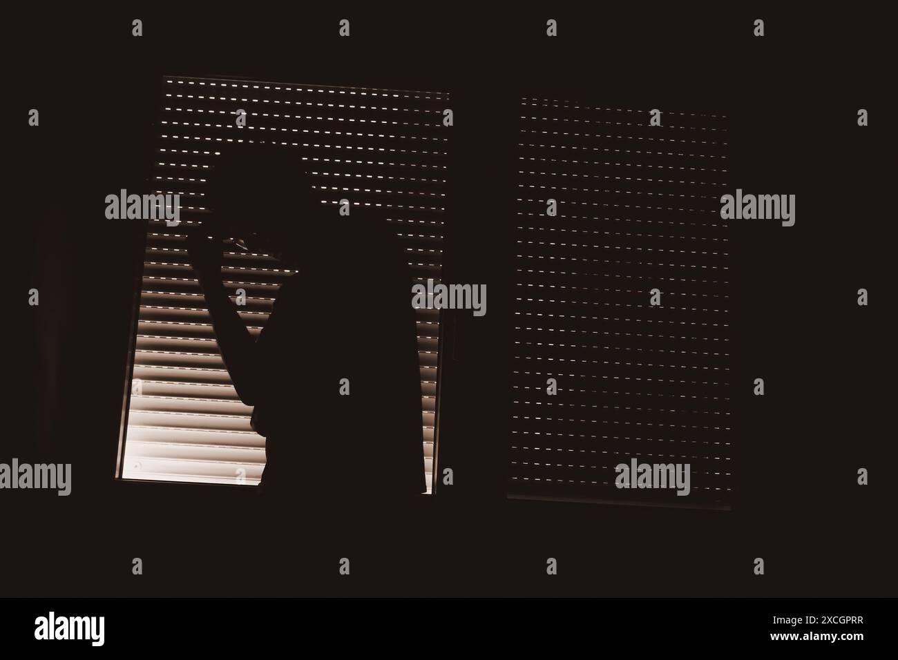 Concept de trouble de la personnalité paranoïaque, silhouette de personne masculine par la fenêtre avec volets fermés, touche basse Banque D'Images
