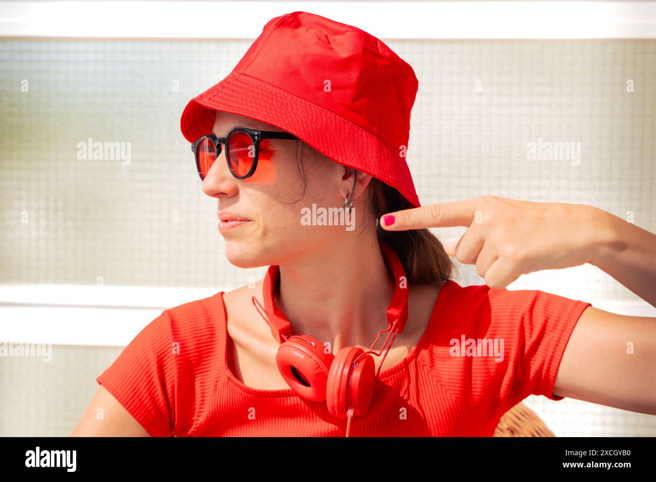 Une jeune femme portant des lunettes de soleil est assise, pointant son doigt sur le côté. Banque D'Images