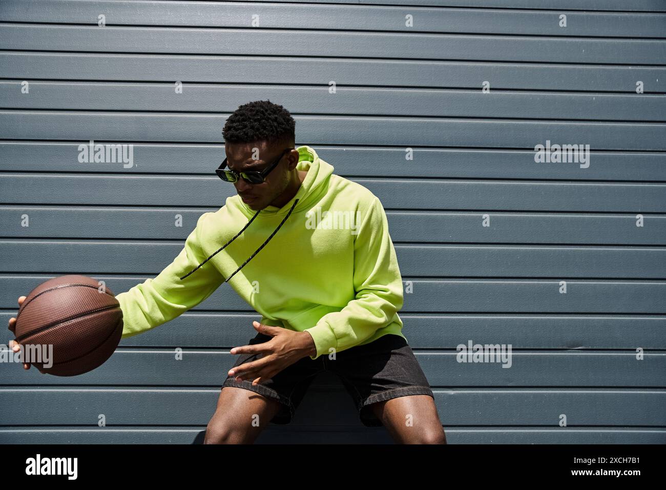 Jeune homme d'ascendance africaine dans un sweat à capuche vert vif tenant un basket-ball. Banque D'Images
