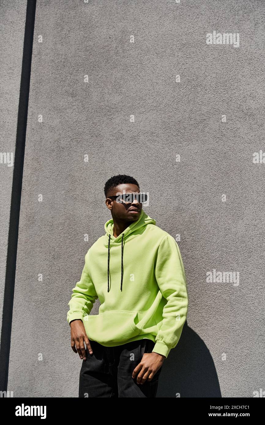 Élégant homme afro-américain en sweat à capuche vert citron appuyé contre un mur. Banque D'Images