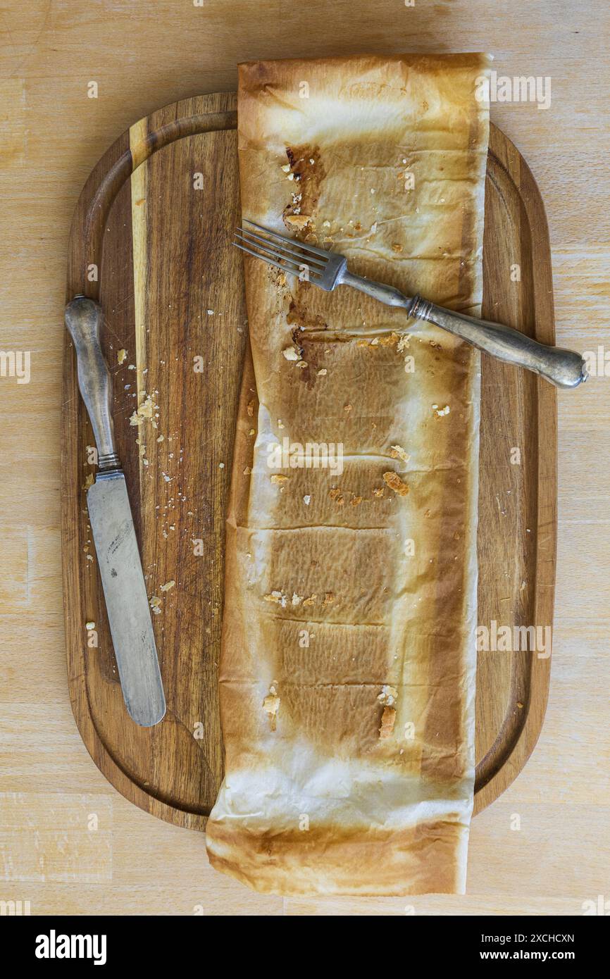 Photographie de table d'une planche à découper en bois d'acacia avec du papier à pâtisserie laissé sur la tarte et fourchette vintage et couteau sur une table en bois Banque D'Images