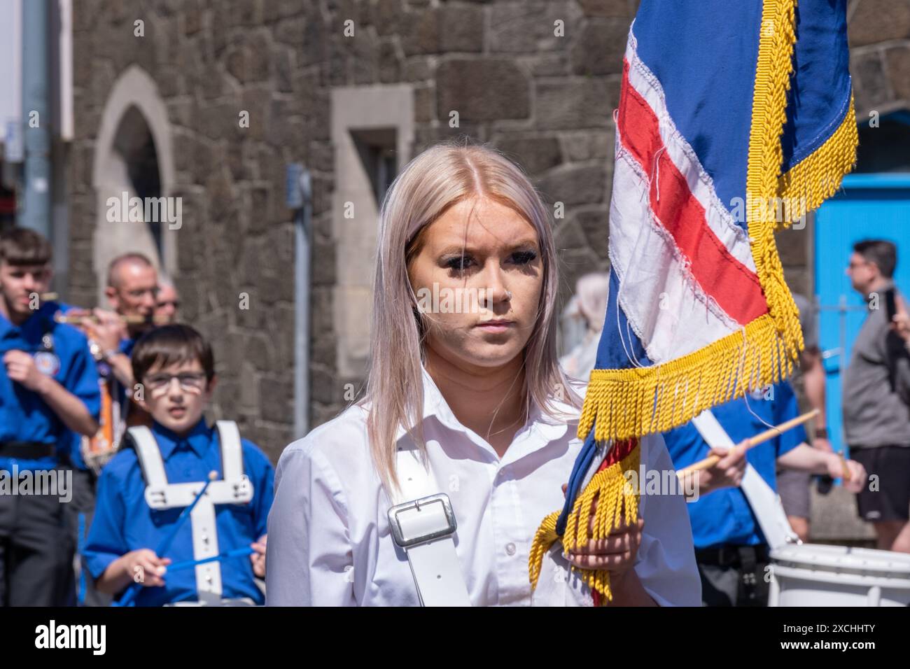 Jeune blonde porte-drapeau féminin avec bande de flûte loyaliste. Portrush, le 1er juin 2024, défilé Junior Orange Order à travers la ville côtière. Banque D'Images