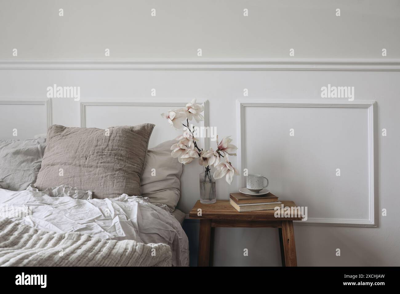 Chambre élégante. Table de nuit en bois avec vase en verre cannelé. Branches de magnolia en fleurs. Tasse de café sur de vieux livres. Intérieur scandinave. Lin Banque D'Images