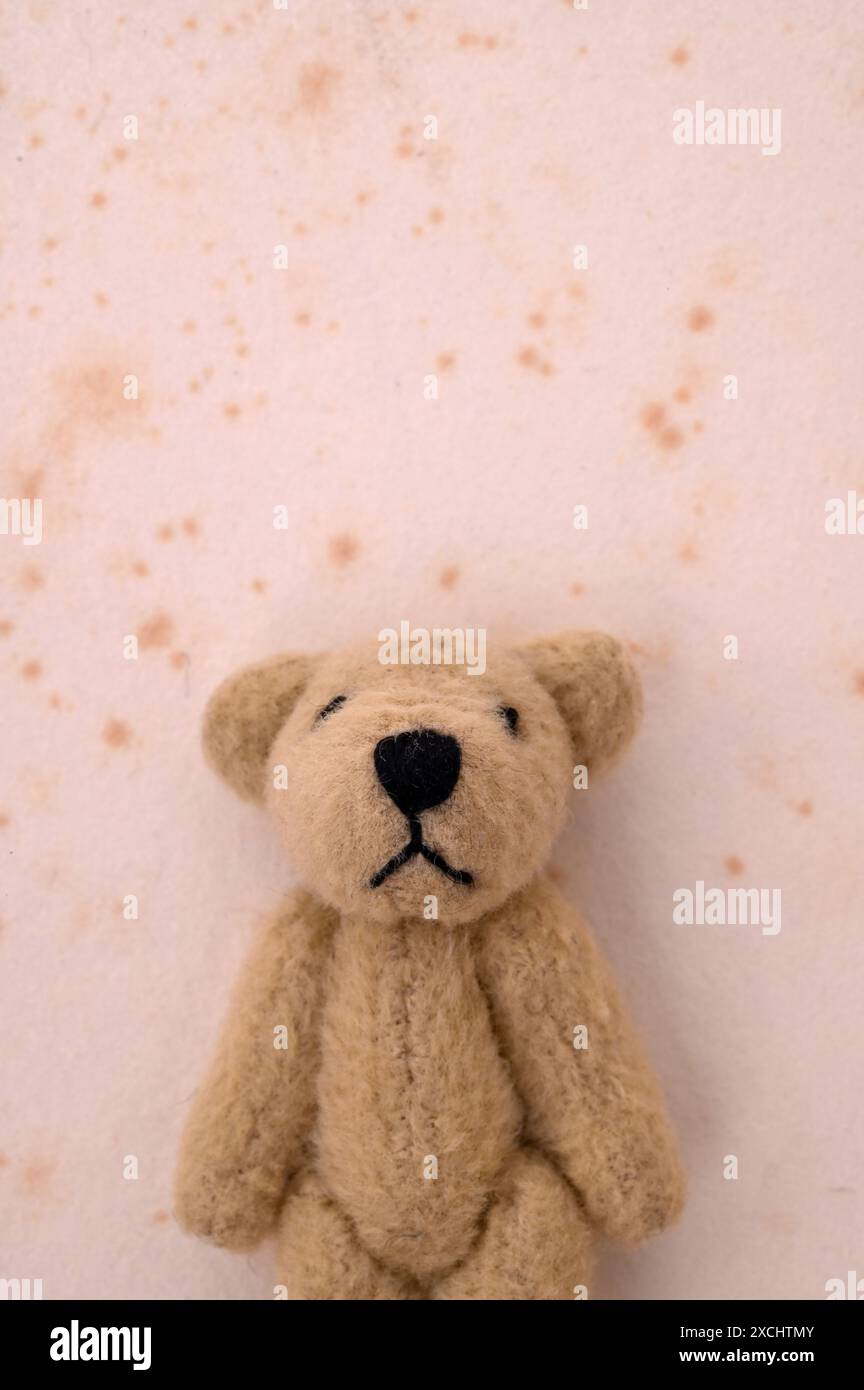 Petit ours en peluche beige avec le visage triste debout devant le mur taché Banque D'Images