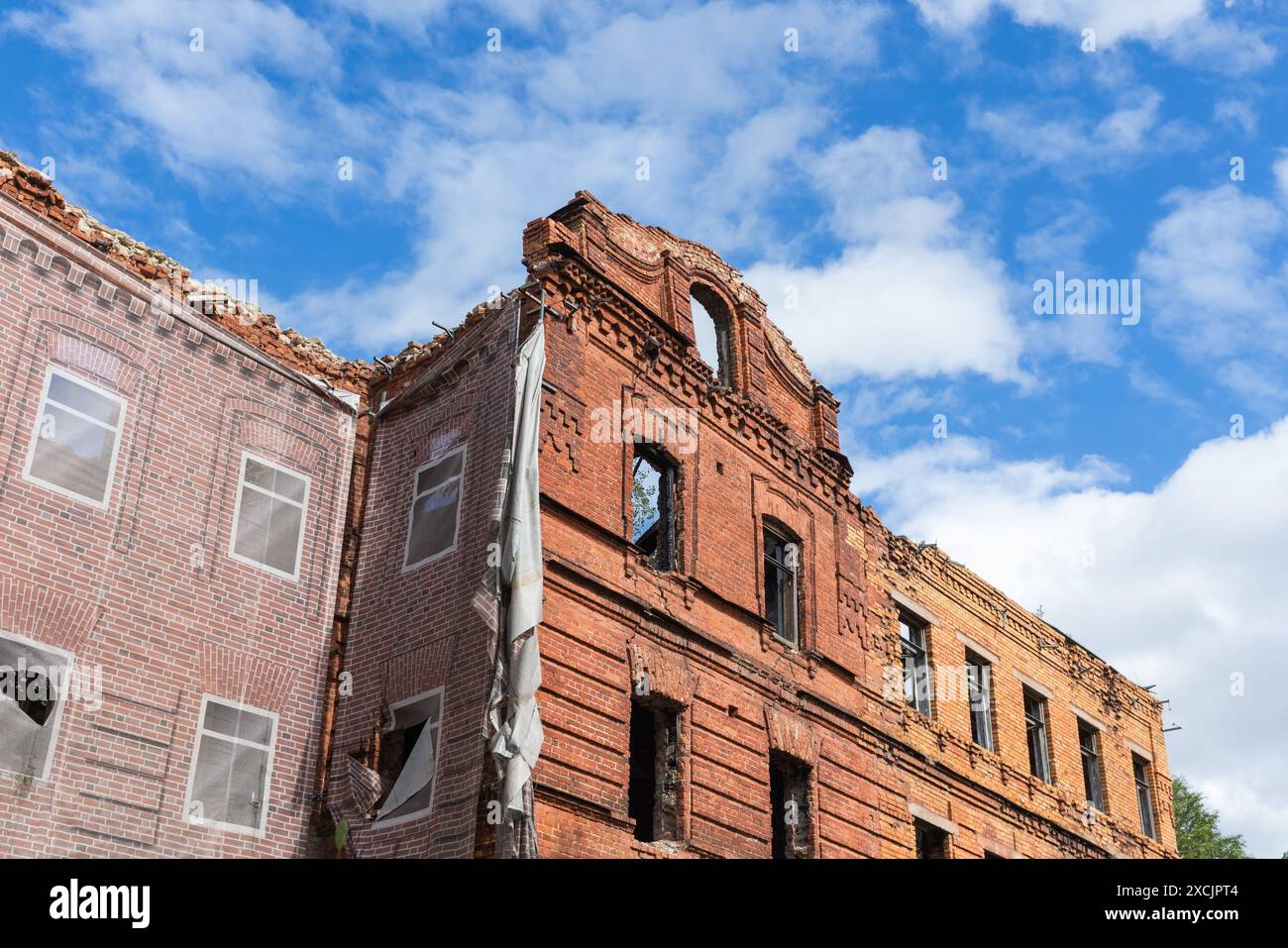 Le bâtiment abandonné en briques rouges est en rénovation, les murs de façade avec des fenêtres vides sont sous le ciel bleu Banque D'Images