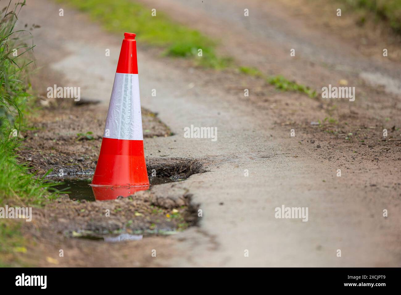 Trou de pot profond dans une voie de campagne britannique remplie d'eau et marquée par un cône de route rouge et blanc vif. Garder les routes britanniques sûres ! Banque D'Images