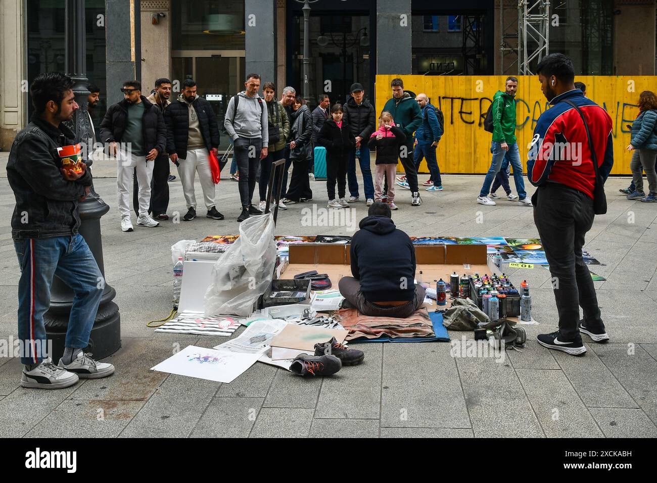 Vue arrière d'un artiste de rue créant des peintures avec des bombes aérosol sur le trottoir dans la Piazza dei Mercanti centrale, avec les gens regardant, Milan, Italie Banque D'Images