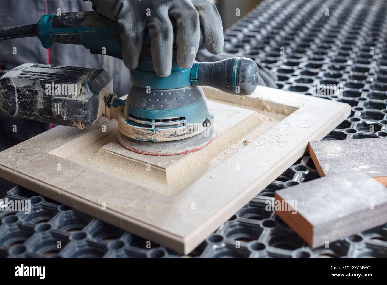 Un menuisier masculin sabre les façades de meubles en bois avec une ponceuse dans une usine de production de meubles, concept de traitement du bois Banque D'Images