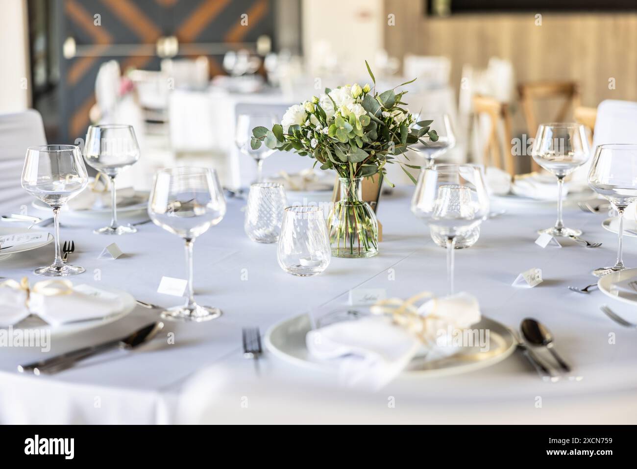 Une table de mariage recouverte d'une nappe blanche, décorée de fleurs, bougies, verres et couverts. Banque D'Images