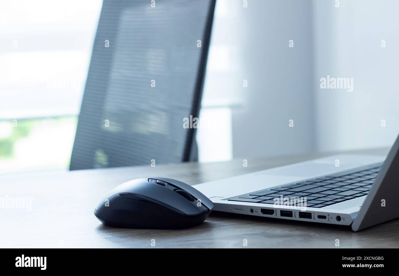 souris d'ordinateur gros plan à proximité ordinateur portable et clavier argenté, chaise et fond de fenêtre, concept de bureau Banque D'Images