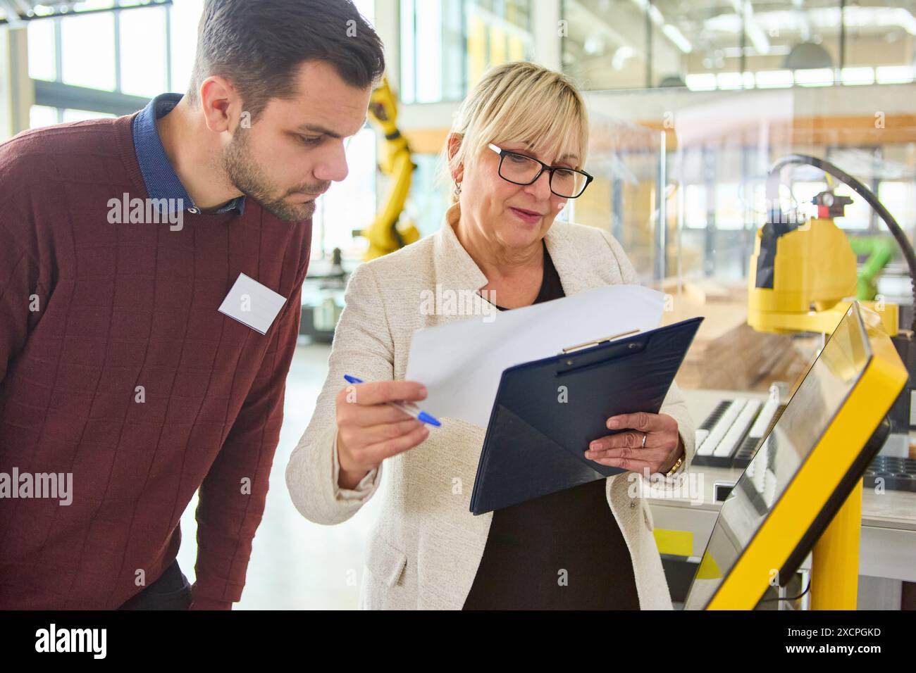 Deux ingénieurs examinent des documents et discutent de la programmation robotique dans un environnement industriel, en se concentrant sur les applications d'automatisation et de production. Banque D'Images