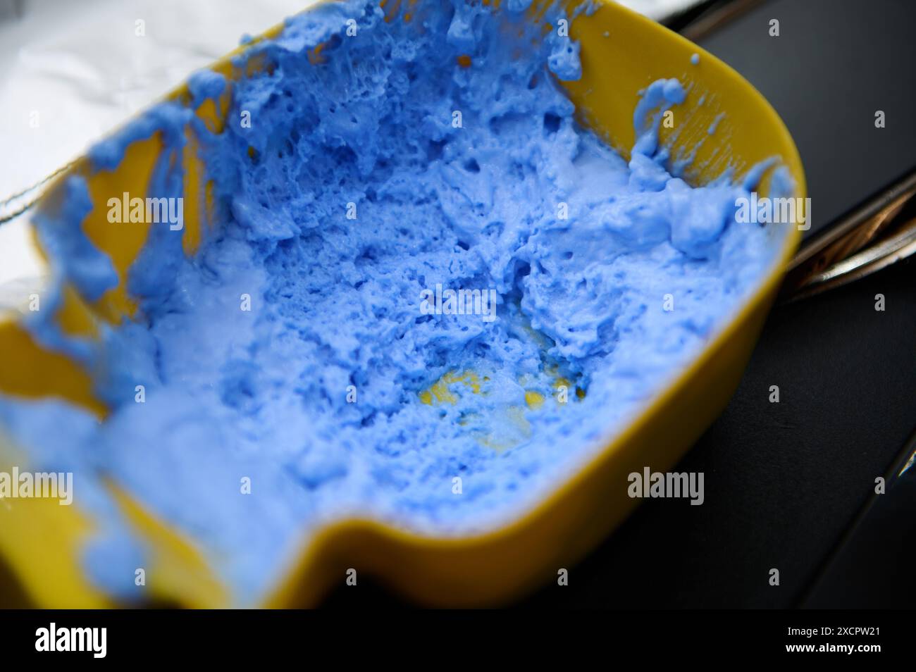 Image en gros plan du mélange bleu de teinture capillaire dans un récipient jaune dans un salon de beauté, prêt pour la coloration des cheveux. Banque D'Images