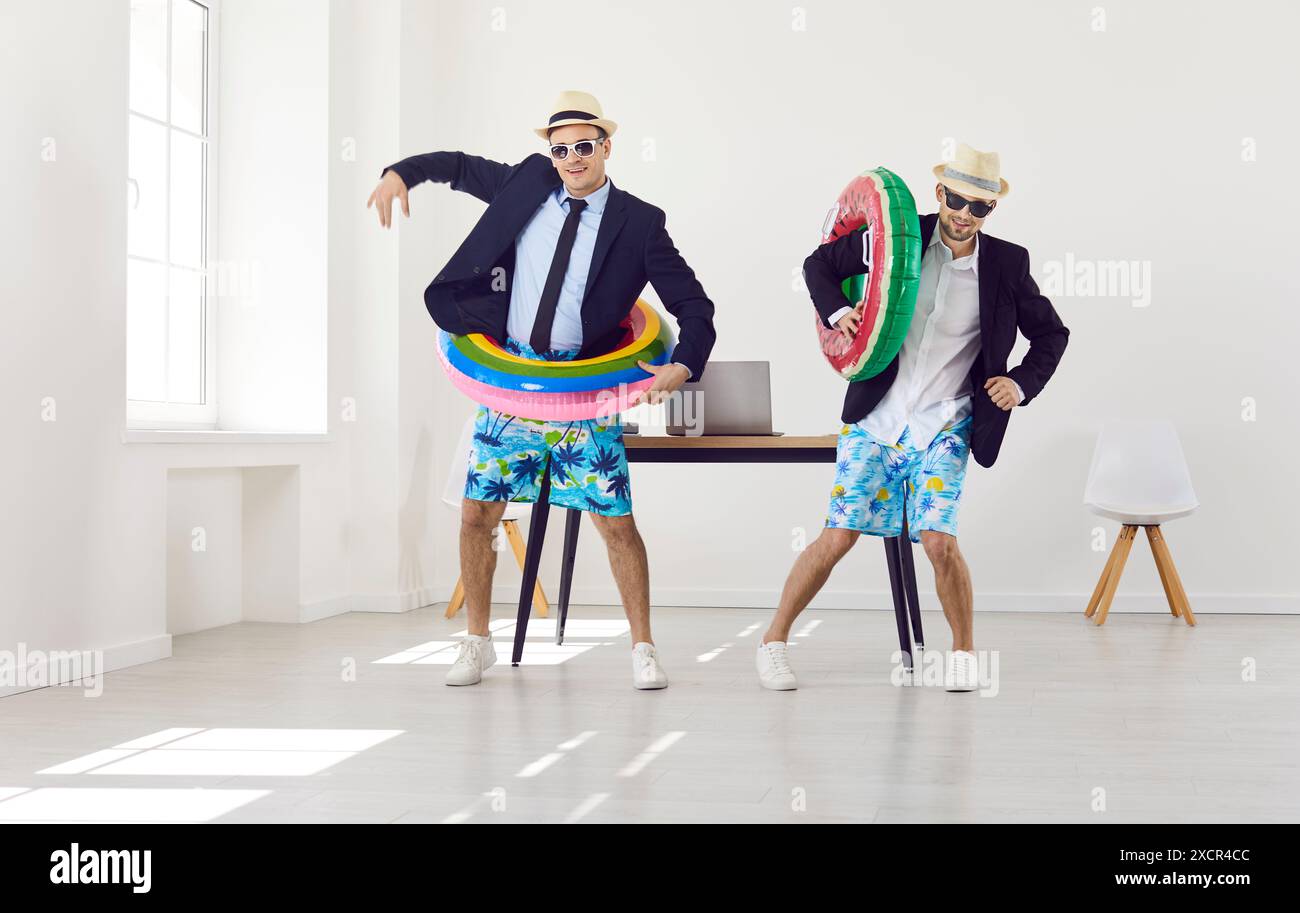 Deux amis heureux prêts pour les vacances d'été dansant avec des anneaux gonflables dans le bureau Banque D'Images