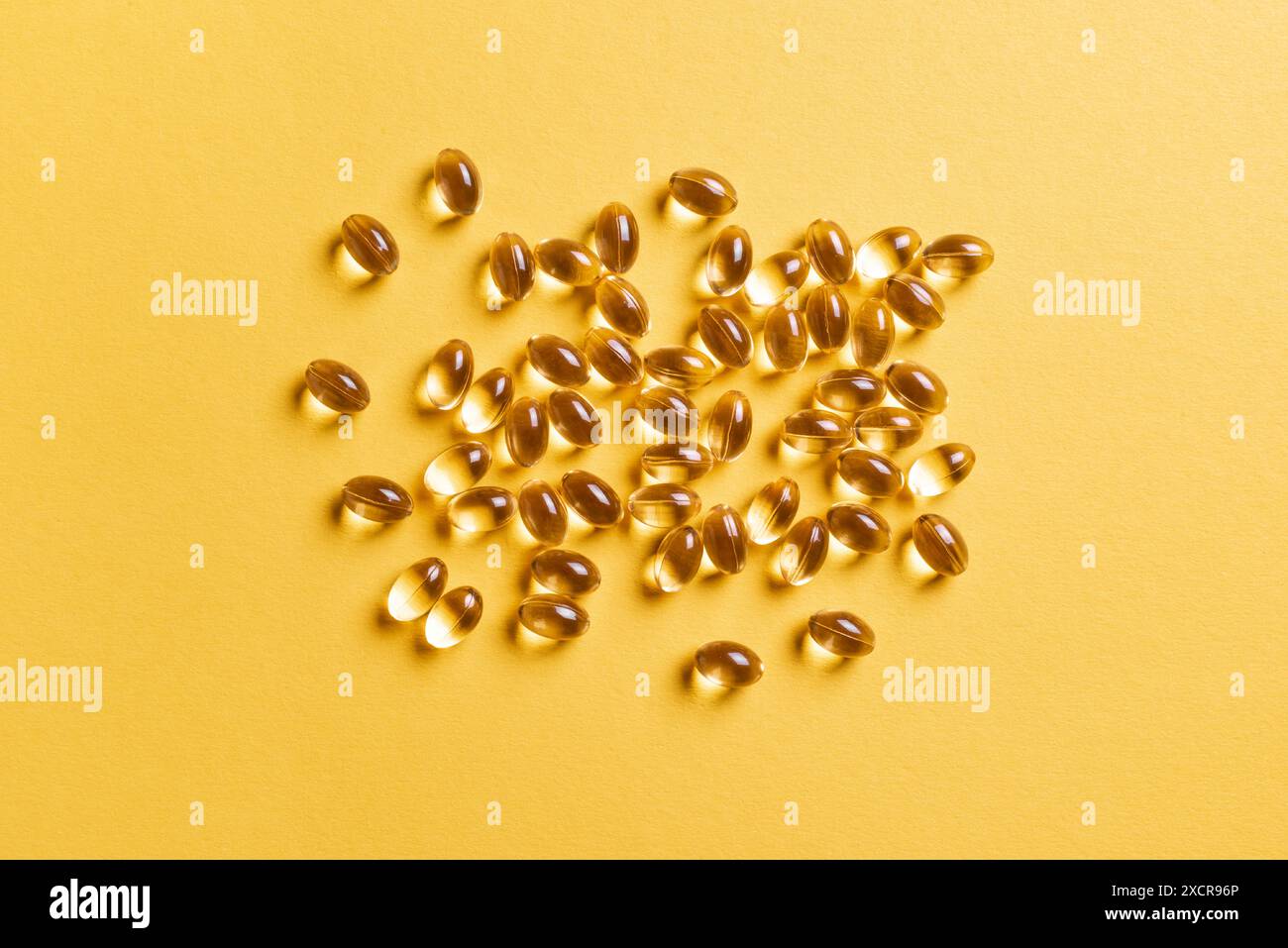 Capsules de vitamine D3 ou capsules d'huile de poisson oméga-3 sur fond jaune, vue de dessus. Tas de softgels dorés avec de l'huile, supplément nutritionnel. Banque D'Images