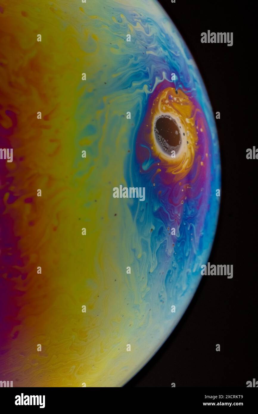 Gros plan, macro plan d'un arc-en-ciel, bulle de savon multicolore avec des couleurs jaune, violet, rose, bleu et vert sur fond noir. Banque D'Images