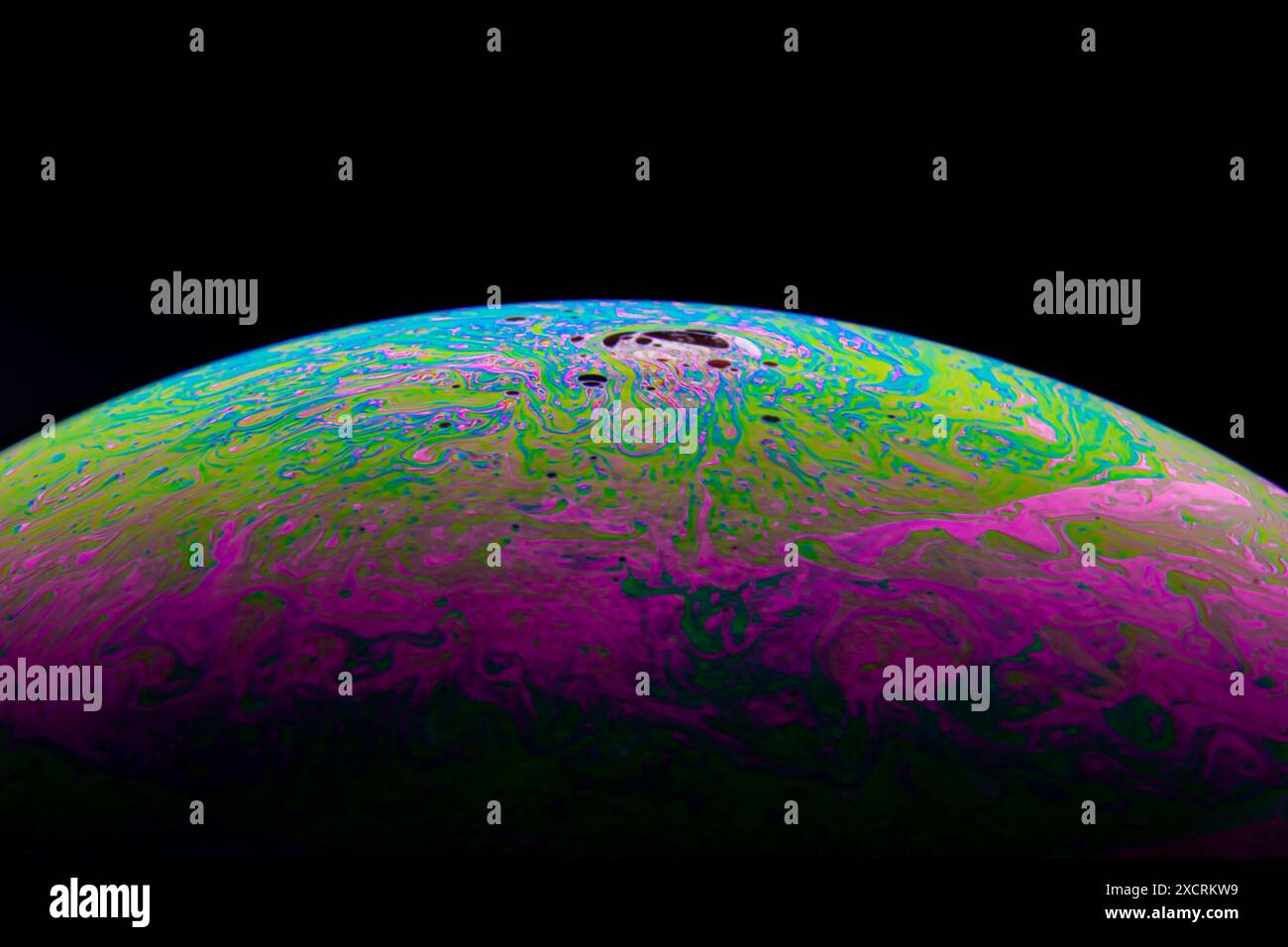 Gros plan, macro plan d'un arc-en-ciel, bulle de savon multicolore avec des couleurs jaune, violet, rose, bleu et vert sur fond noir. Banque D'Images