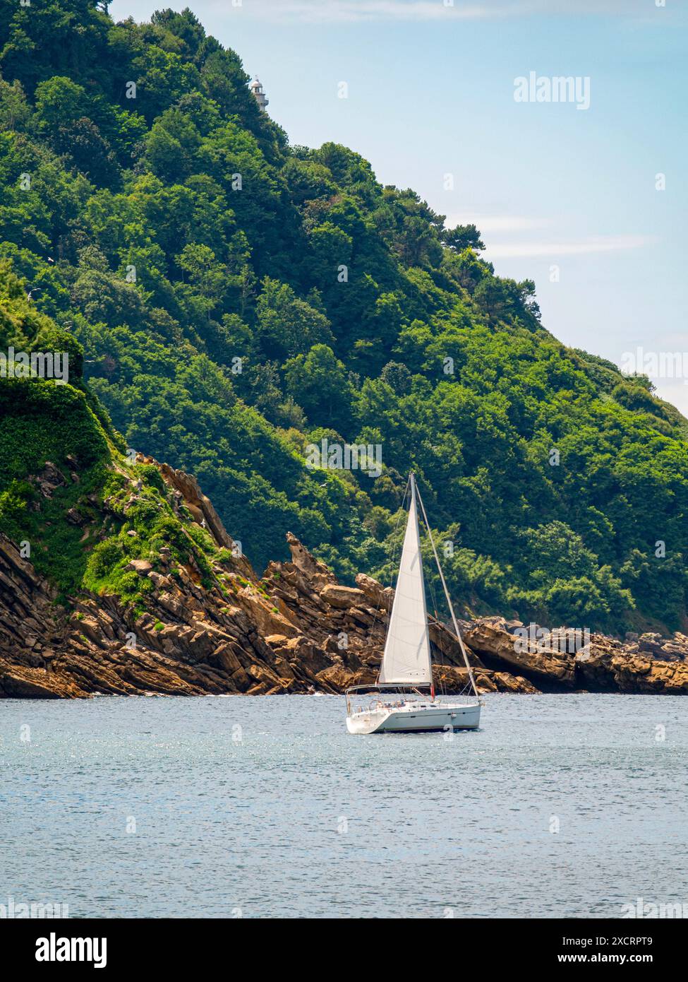 Voilier yacht devant une colline rocheuse couverte d'arbres verts. Banque D'Images