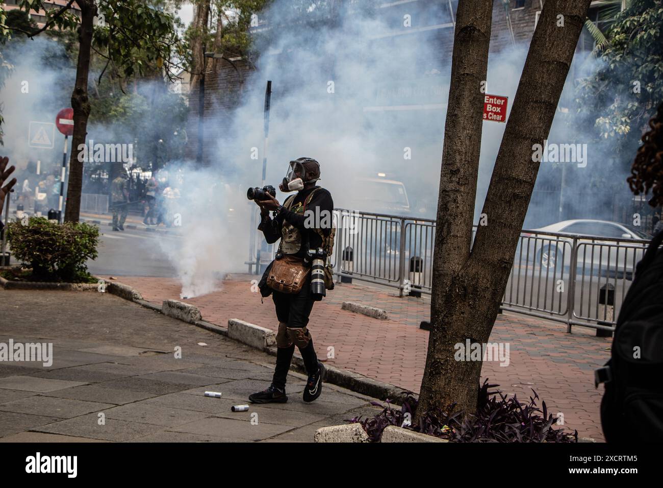 Nairobi, Kenya. 18 juin 2024. Un journaliste prend des photos devant un nuage de fumée provenant de cartouches lacrymogènes lobées contre les manifestants lors d’une manifestation contre le projet de loi de finances 2024 dans les rues de Nairobi. Le projet de loi propose plusieurs nouvelles taxes, dont une taxe de circulation sur les véhicules automobiles, une taxe sur les transferts de fonds, une taxe écologique et des droits d'accise sur le pain et l'huile de cuisson. La manifestation baptisée #RejectTheFinanceBill2024 a lieu alors que le projet de loi est déposé, avec des manifestants exhortant les membres du parlement à rejeter les dispositions litigieuses. Crédit : SOPA images Limited/Alamy Live News Banque D'Images