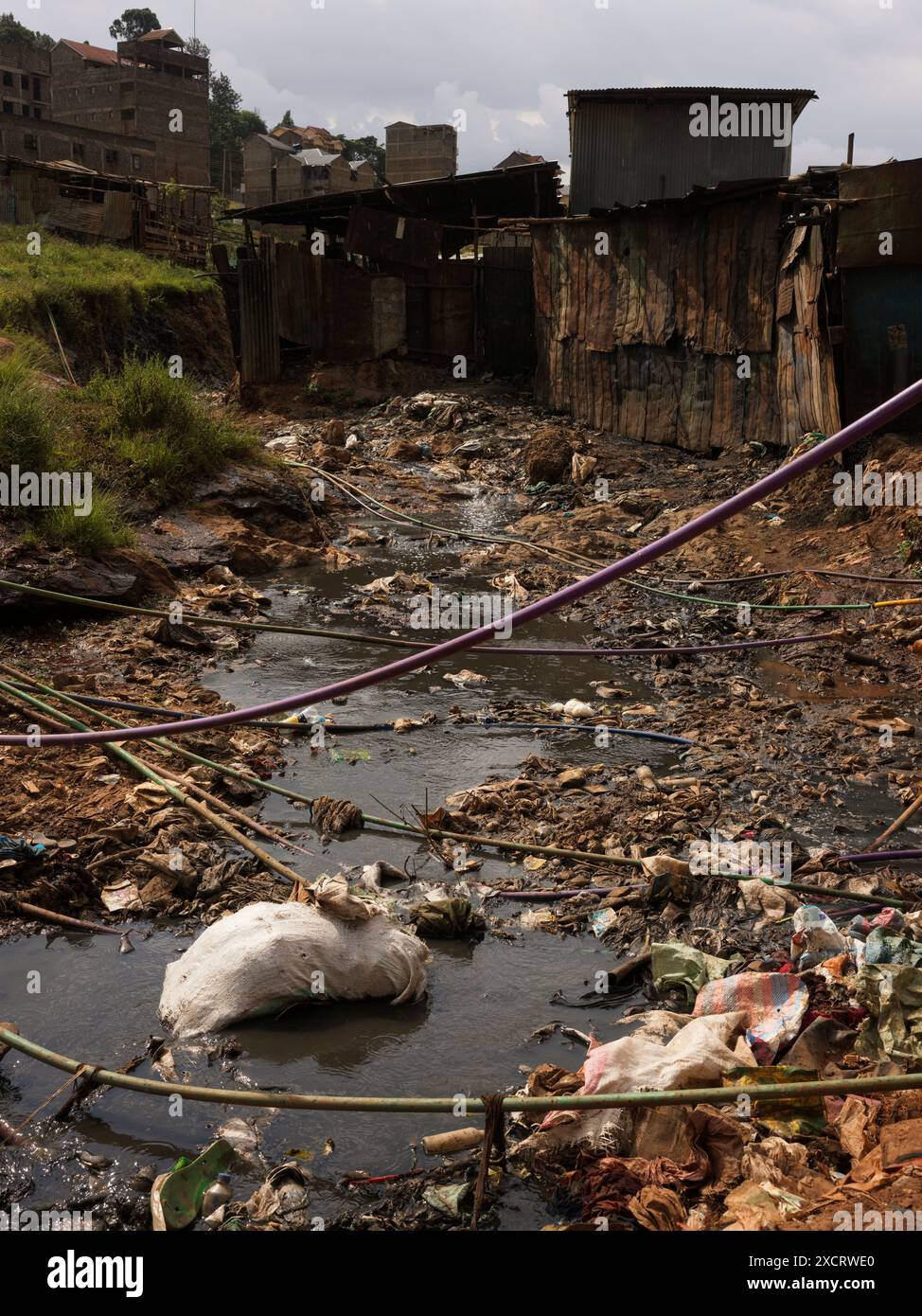 Un ruisseau rempli d’ordures et de déchets traversant le bidonville de Kibera à Nairobi avec des conduites d’alimentation en eau traversant d’un côté à l’autre Banque D'Images