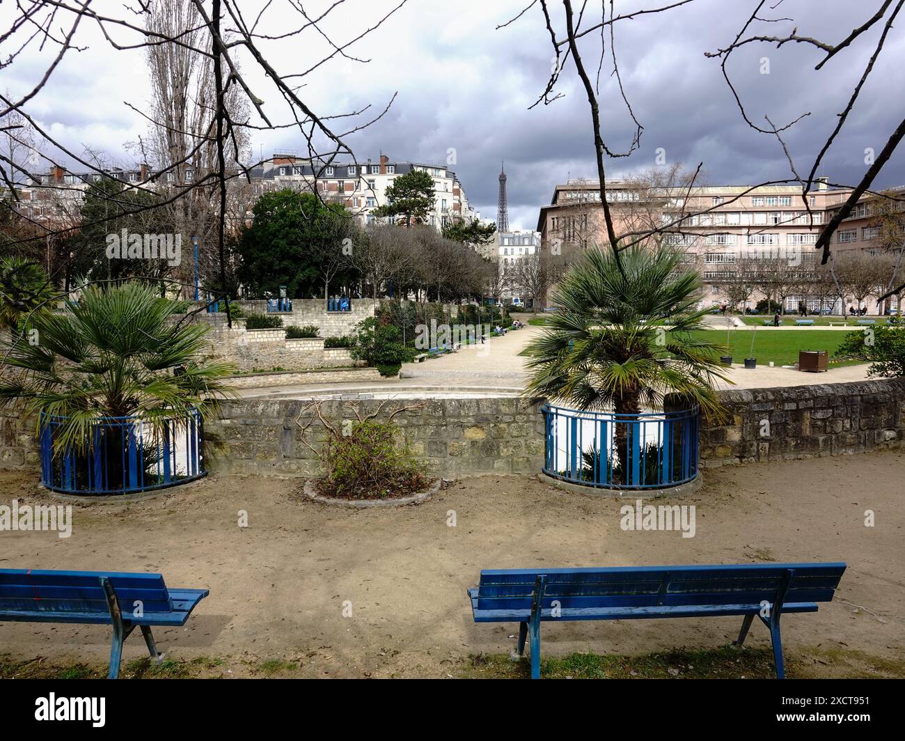 Vue de la Tour Eiffel à distance à travers la place Saint-Lambert, comme les gens se détendent sur les bancs du parc le jour nuageux de mars, 15ème arrondissement, Paris, France. Banque D'Images