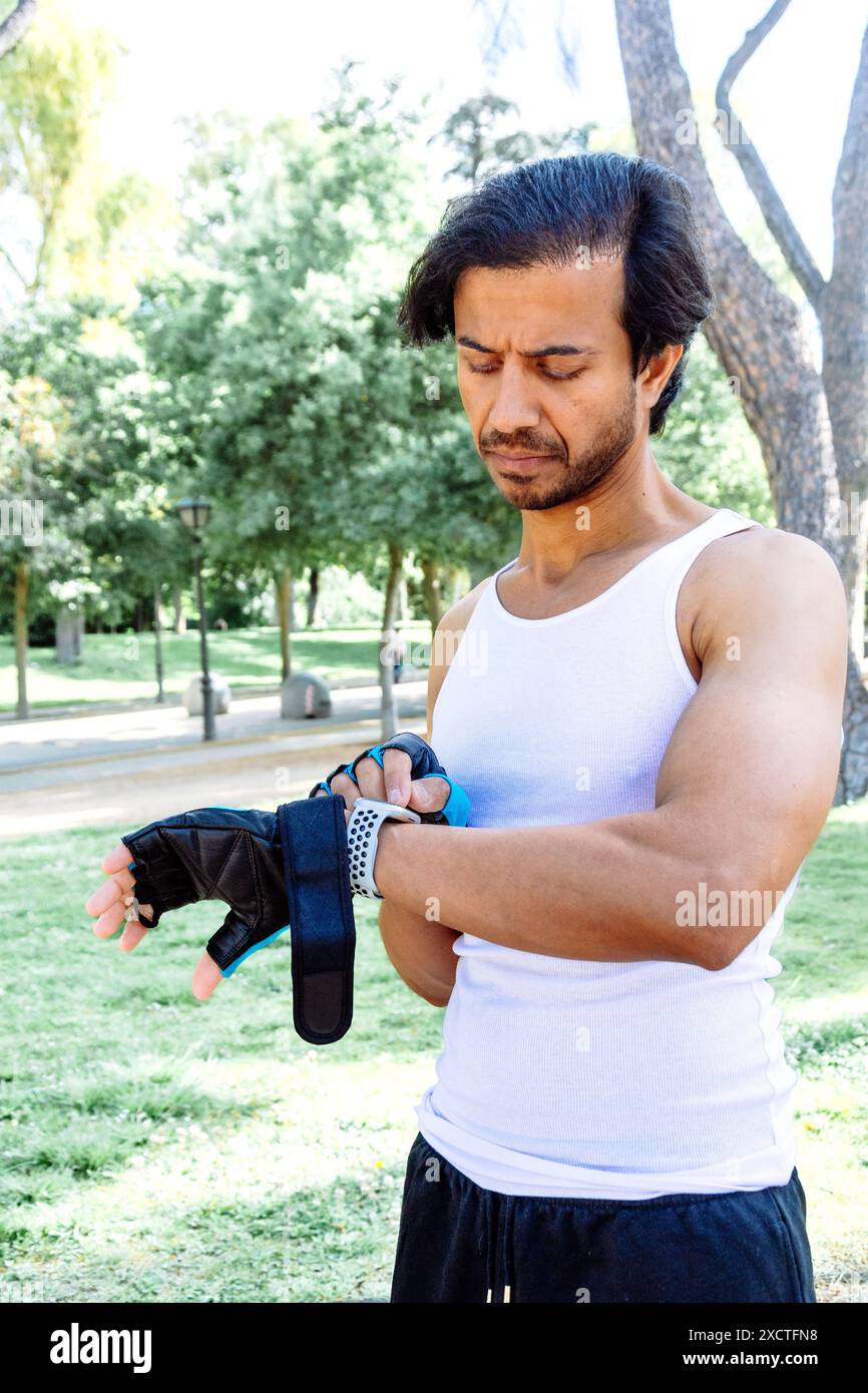 Un homme dans un débardeur blanc et un short noir porte un bracelet bleu. Il est debout dans un parc et il se concentre sur quelque chose Banque D'Images Un homme dans un débardeur blanc et un short noir porte un bracelet bleu. Il est debout dans un parc et il se concentre sur quelque chose Banque D'Images