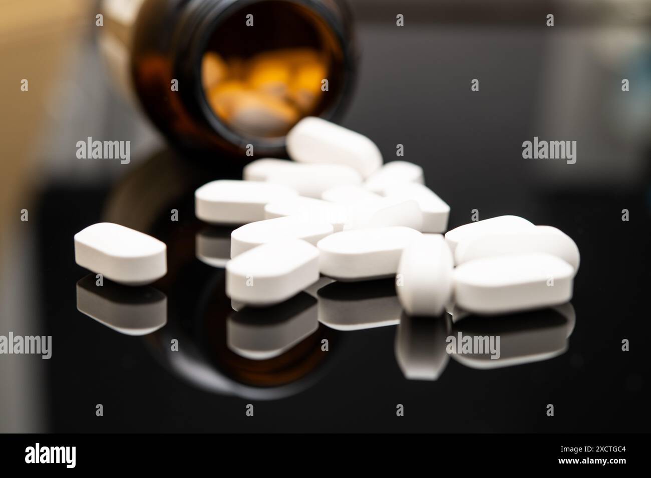 Vue rapprochée de comprimés opioïdes blancs de forme ovale renversés d’un flacon de prescription foncé sur une surface noire réfléchissante, mettant en évidence le fentanyl Banque D'Images