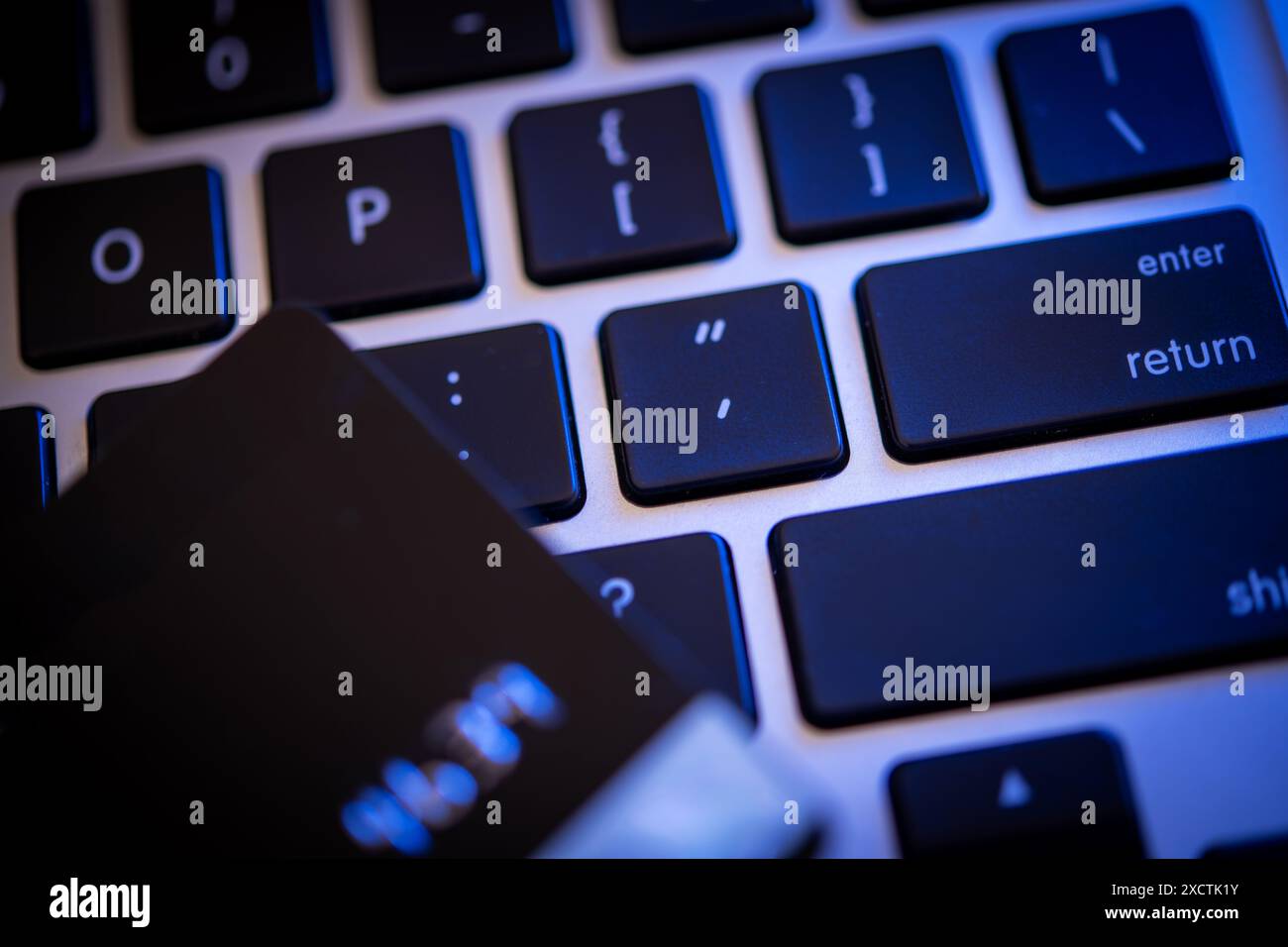 Une carte de crédit repose sur les touches d'un clavier d'ordinateur rétroéclairé, illustrant les thèmes de la cybersécurité, du vol d'identité et de la sécurité financière en ligne. Banque D'Images