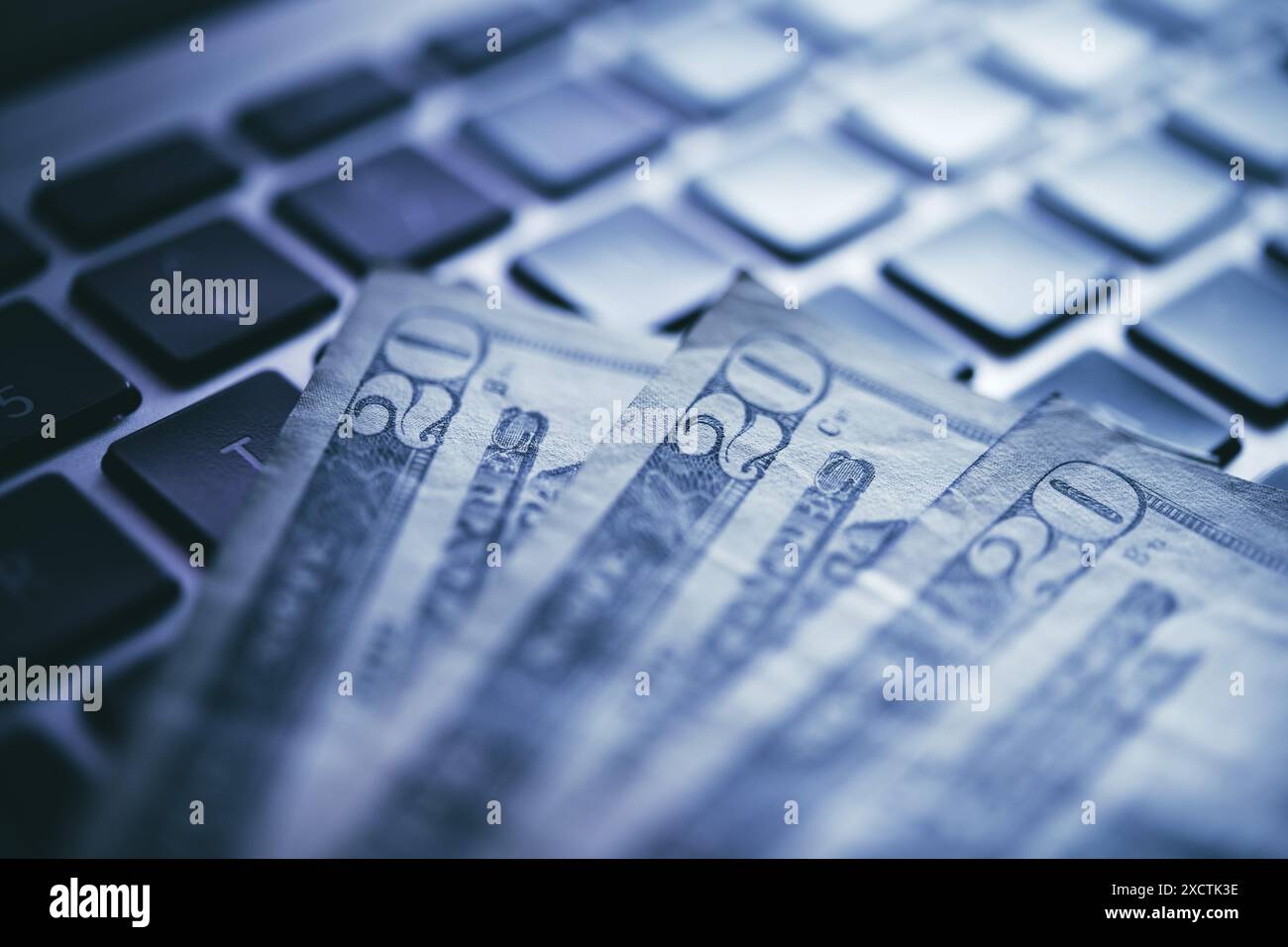 Un gros plan capture des billets de 20 dollars américains disposés sur un clavier moderne d'ordinateur portable, mettant l'accent sur les thèmes des transactions financières en ligne et du numérique Banque D'Images