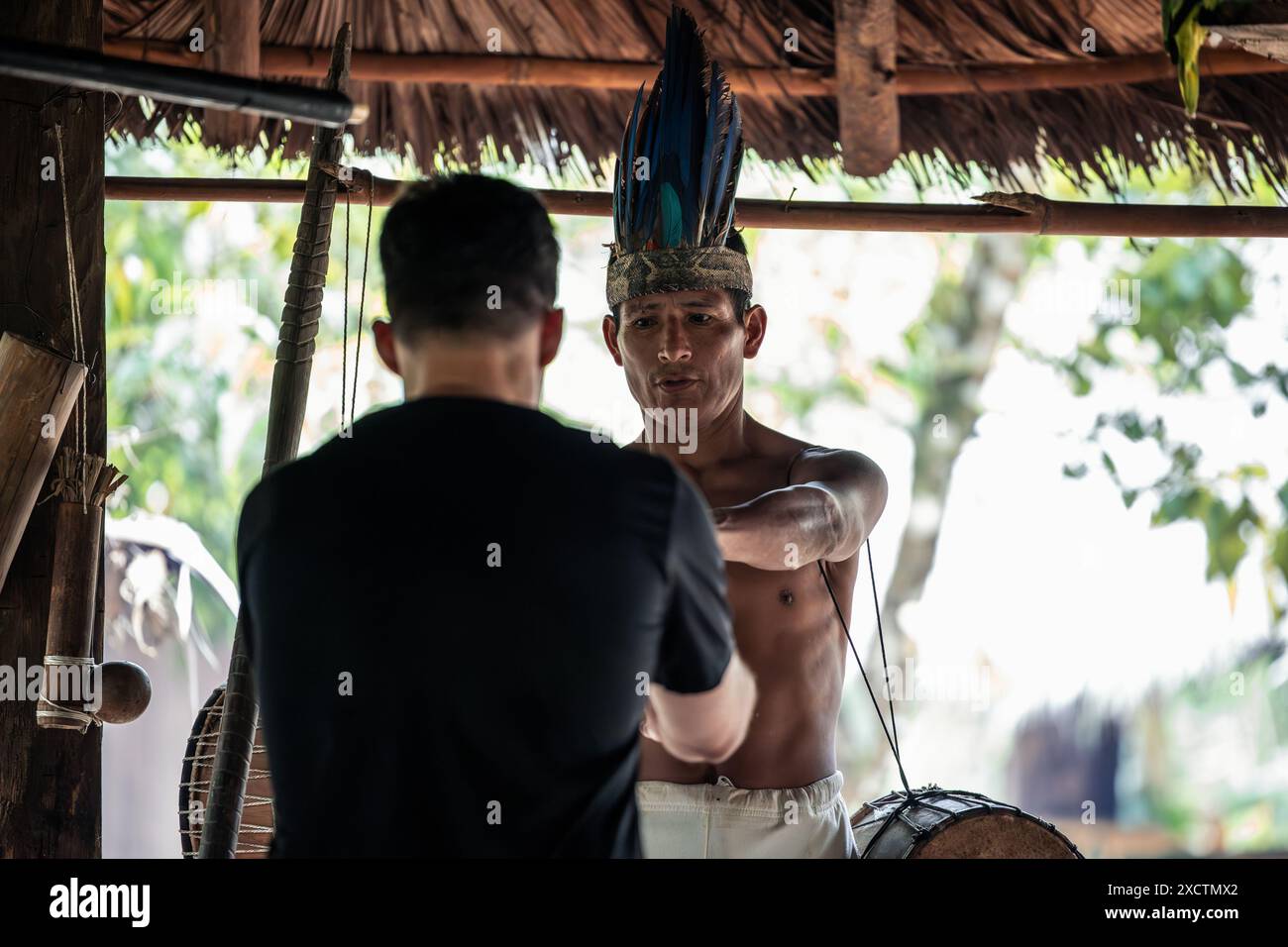 Un membre indigène de la tribu Wayuri est vu en train de remettre un tambour chamanique à un touriste dans la jungle équatorienne. Cette image capture un moment d'échange culturel, Banque D'Images