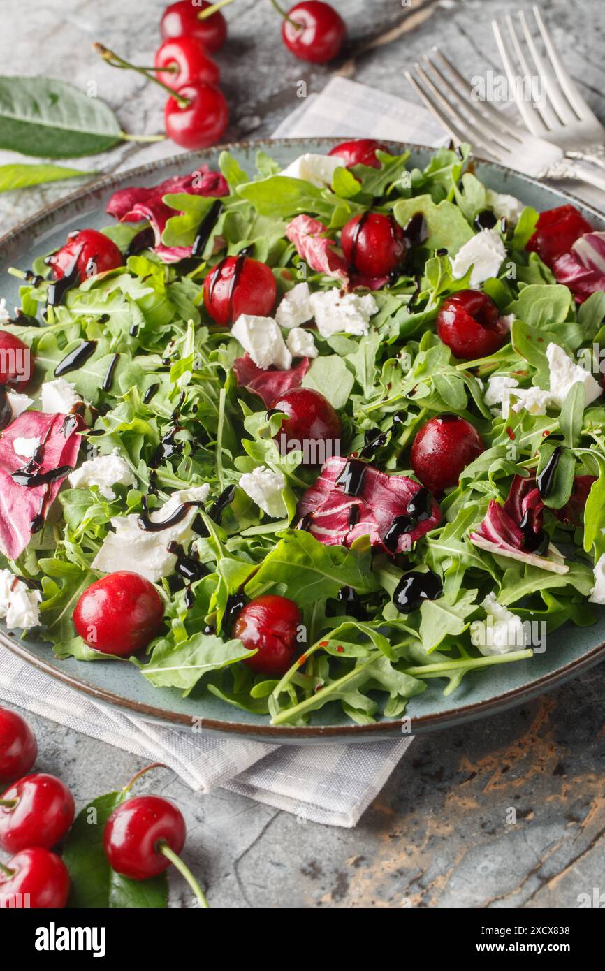 Cerise marinée, fromage de chèvre et salade de roquette avec sauce balsamique gros plan dans une assiette sur la table. Vertical Banque D'Images