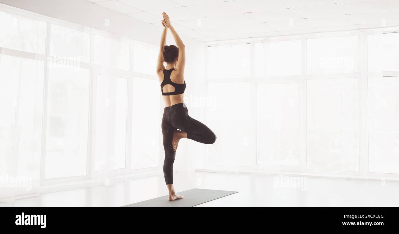 Femme pratiquant le yoga dans un studio spacieux pendant la matinée, vue arrière Banque D'Images