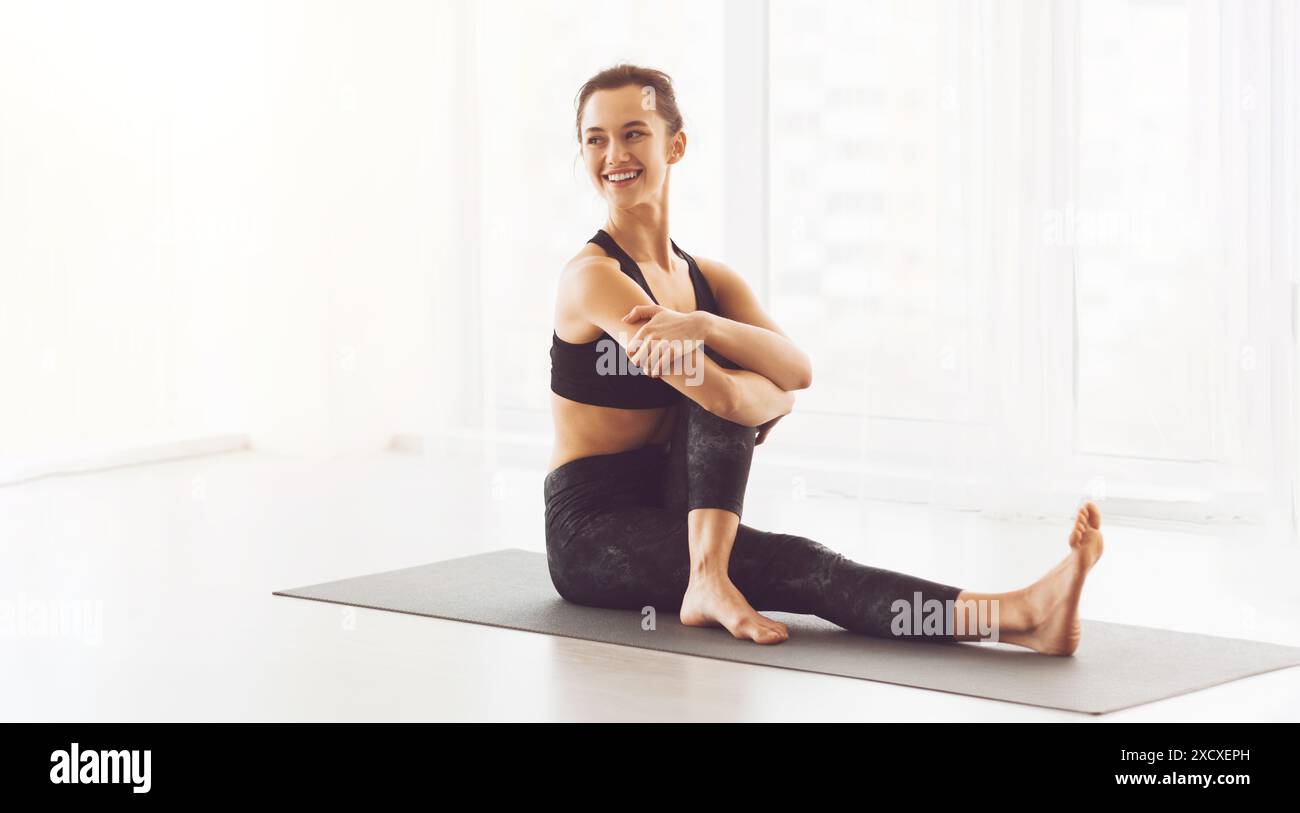 Jeune femme pratiquant le yoga dans une salle ensoleillée, profitant de l'entraînement Banque D'Images