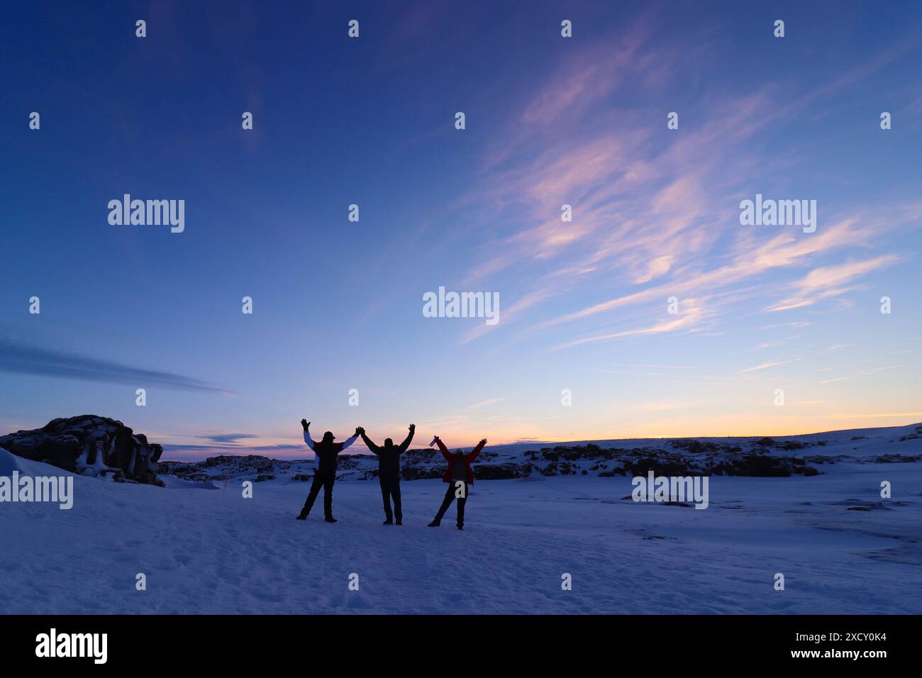 Coucher de soleil en Islande avec trois amis s'amusant dans la neige. trois silhouettes de personnes avec leurs bras levés dans un paysage hivernal. Banque D'Images