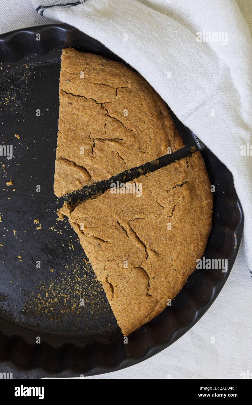 Photographie à plat de Scone d'orge estonien traditionnel (Odrakarask) tranches restantes dans une forme de cuisson en céramique noire avec un torchon de cuisine blanc Banque D'Images
