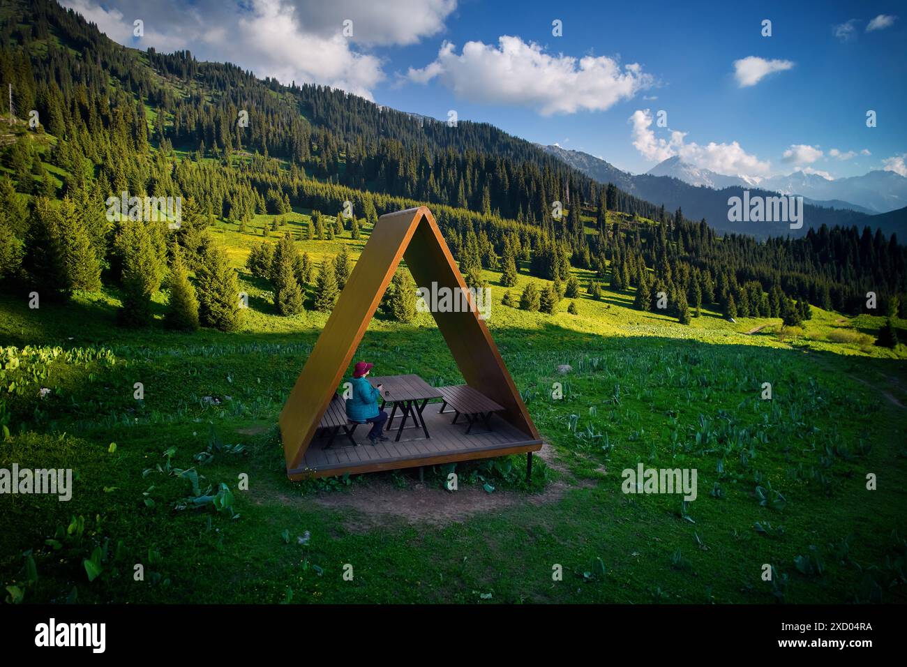 Touriste randonneur femme en veste bleue prendre un repos dans la maison d'été avec toit de triangle au drone aérien beau paysage de montagne sauvage et Fores d'épicéa Banque D'Images