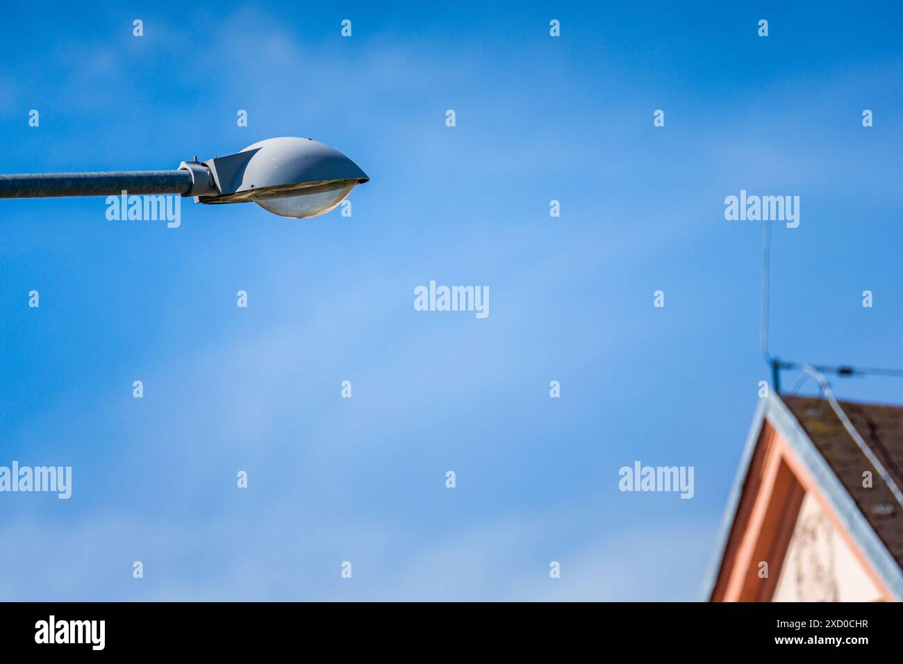 Lampadaire contre ciel bleu clair avec toit de maison en arrière-plan Banque D'Images