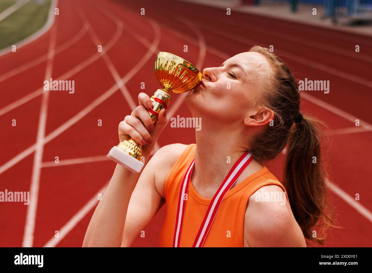 Vainqueur féminin en uniforme sportif embrasse la coupe et célèbre la victoire en compétition d'athlétisme, Sports, concept de victoire. Banque D'Images