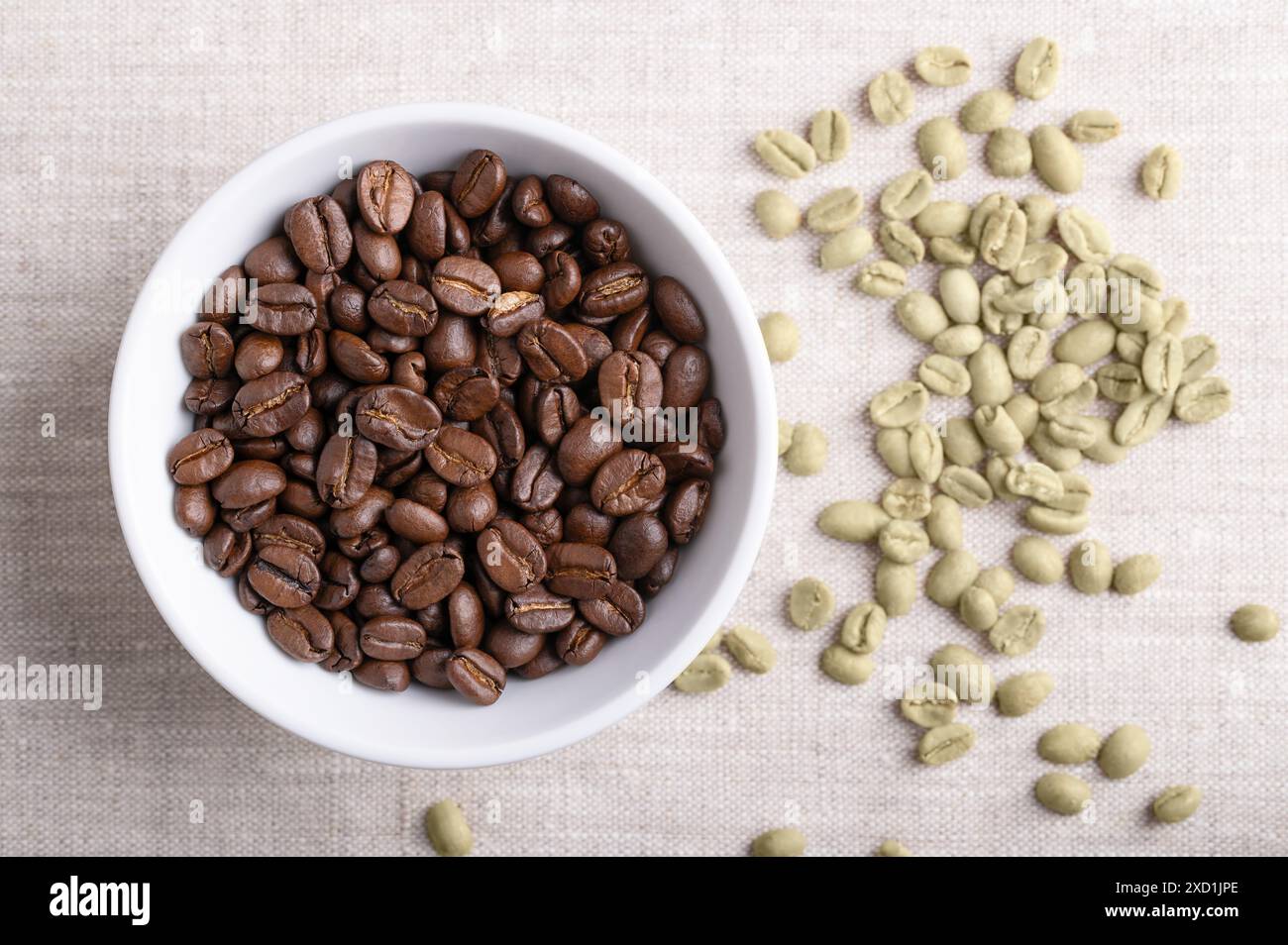 Grains de café torréfiés dans un bol blanc sur tissu de lin. Sur la droite, grains de café Arabica vert non torréfiés, graines de baies de Coffea arabica. Banque D'Images