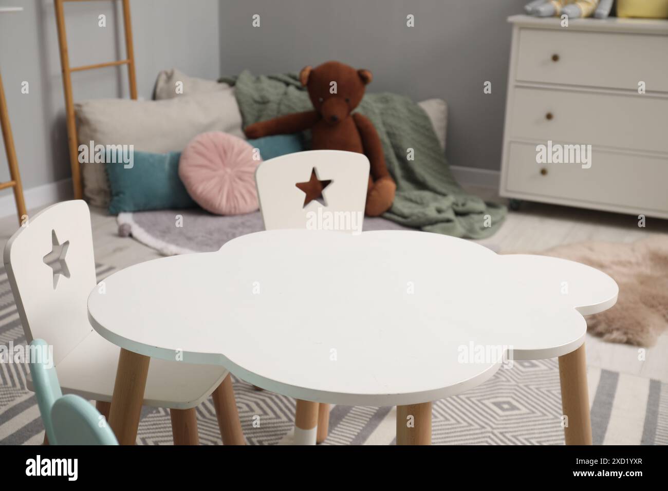 Intérieur élégant de la chambre d'enfant avec table, chaises, ours jouet et commode Banque D'Images