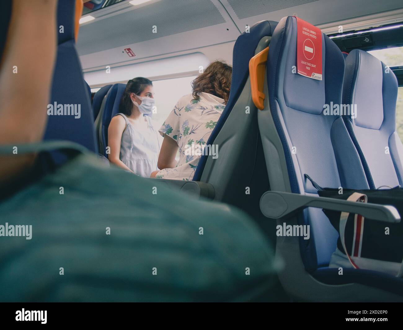 Une jeune femme portant un masque protecteur voyage en train et s'assoit à côté d'un autre passager Banque D'Images