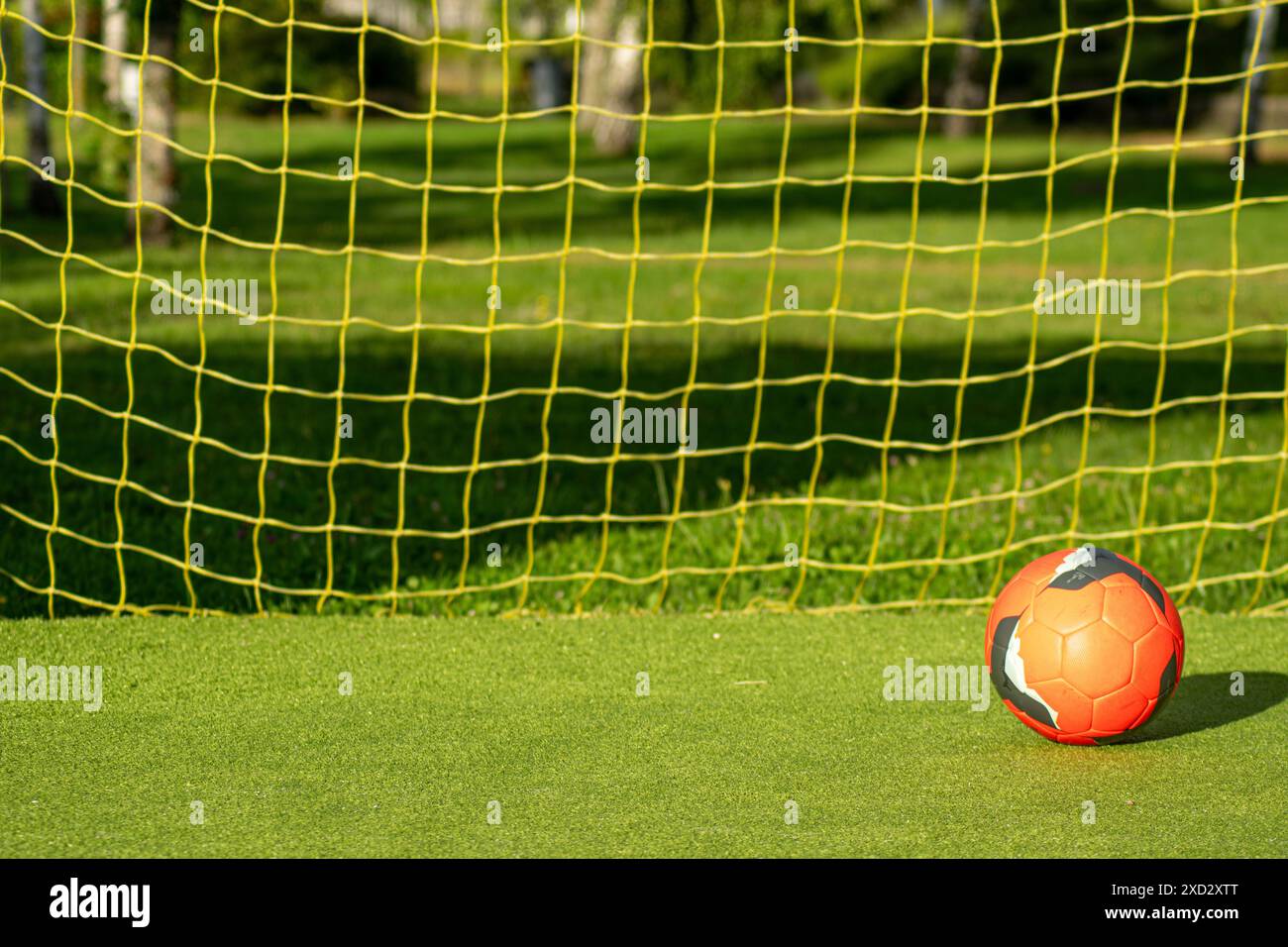 ballon de football rouge avec le filet jaune d'un but sur un terrain de football en gazon artificiel Banque D'Images