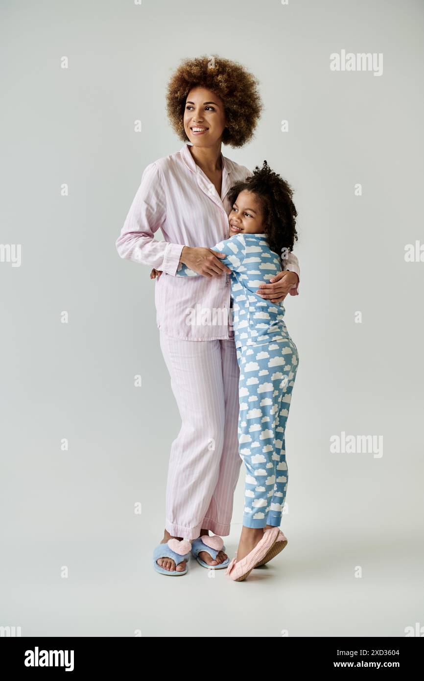 Heureuse mère afro-américaine et fille portant un pyjama, s'embrassant sur un fond gris. Banque D'Images
