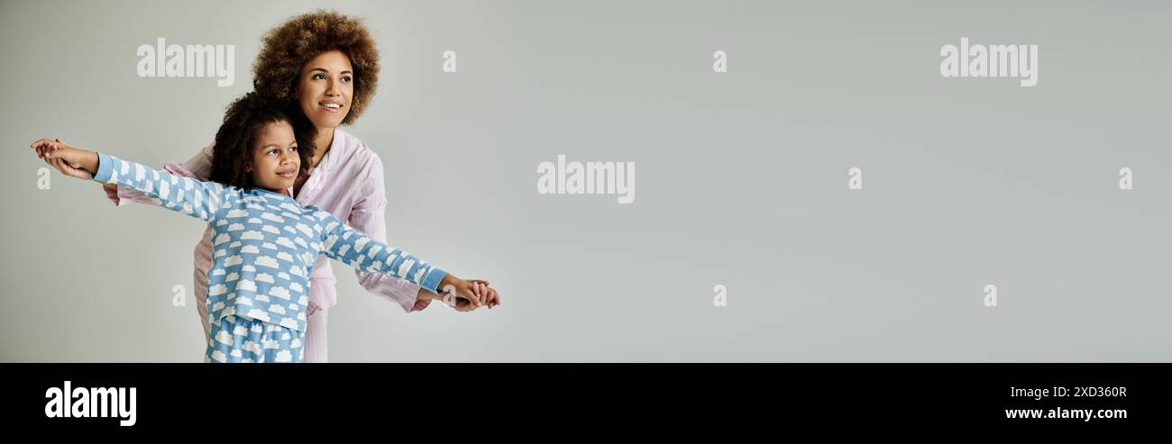 Une mère afro-américaine et sa fille souriantes en pyjama assorti sur un fond gris. Banque D'Images