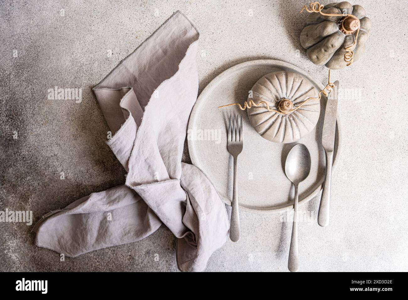 Un plat automnal de bon goût avec une table aux tons neutres avec une citrouille décorative, des assiettes grises et une serviette en lin, idéal pour une décoration saisonnière Banque D'Images