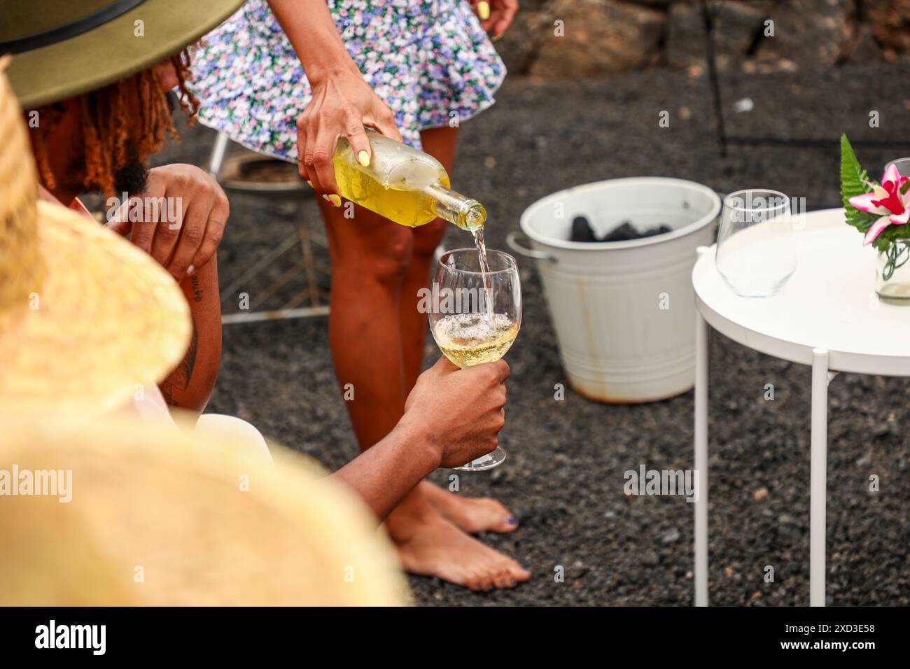 Une femme taillée méconnaissable verse du vin blanc dans un verre tenu par un homme anonyme lors d'un événement social en plein air. Les deux sont des vues partielles et non recog Banque D'Images