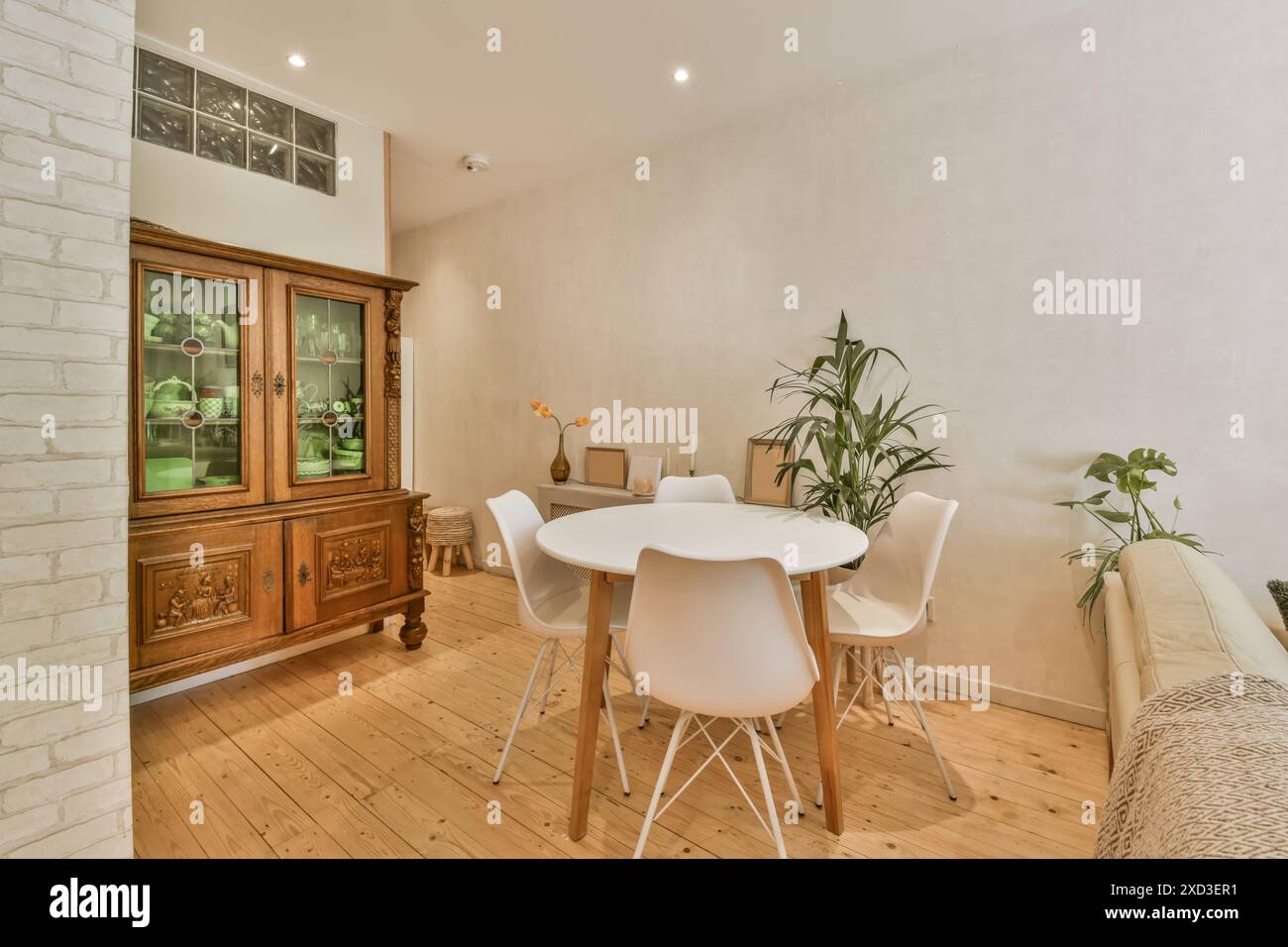 Salle à manger confortable avec une table blanche, des chaises modernes et une armoire en bois classique, complétée par des plantes d'intérieur pour une ambiance fraîche Banque D'Images